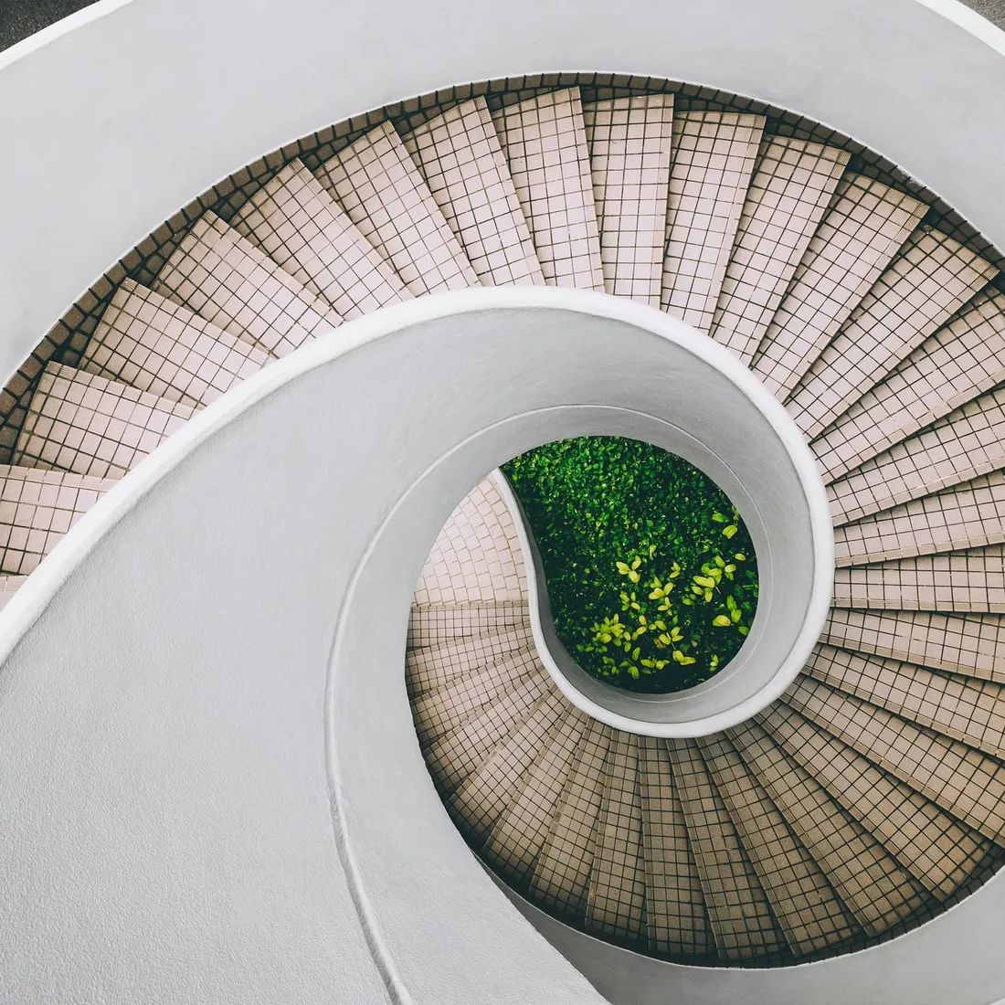 A concrete spiral stair winding down through a pale, top-lit shaft