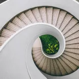 A concrete spiral stair winding down through a pale, top-lit shaft