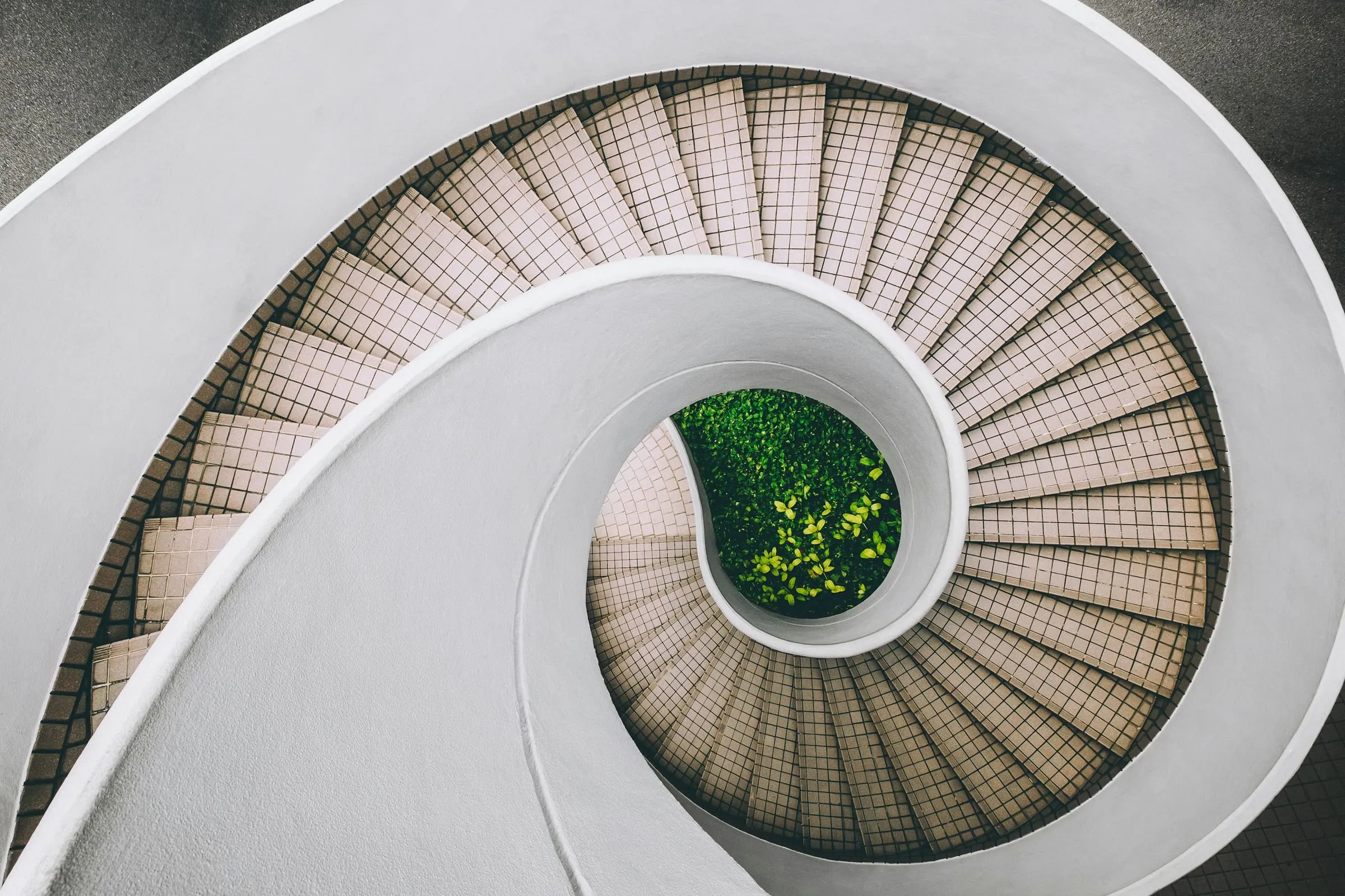 A concrete spiral stair winding down through a pale, top-lit shaft